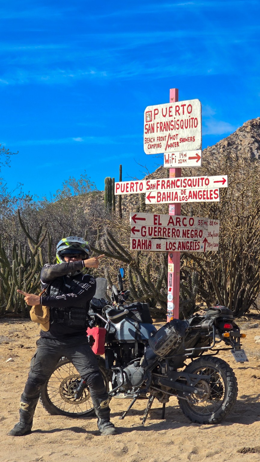 Piloto junto a su motocicleta y los señalamientos hacia Bahía de los Ángeles y Puerto San Francisquito