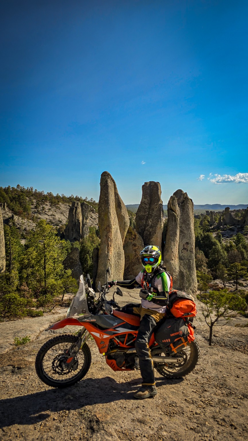 Piloto sobre su motocicleta frente a grandes formaciones rocosas de la sierra