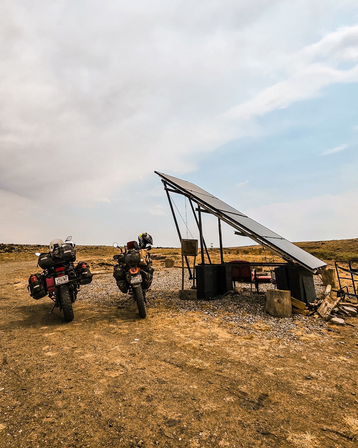 Dos motocicletas de la expedición Continental Divide junto a un panel solar en una parada rural