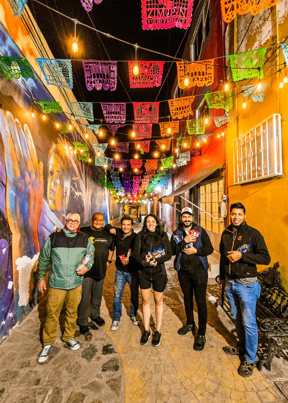 Grupo de viajeros bajo luces y papel picado en una calle por la noche