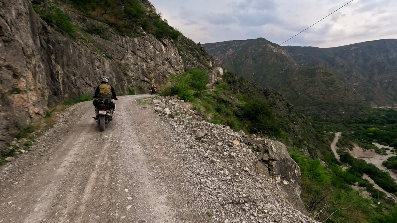 Motociclista recorriendo un camino de sierra junto a un valle entre montañas